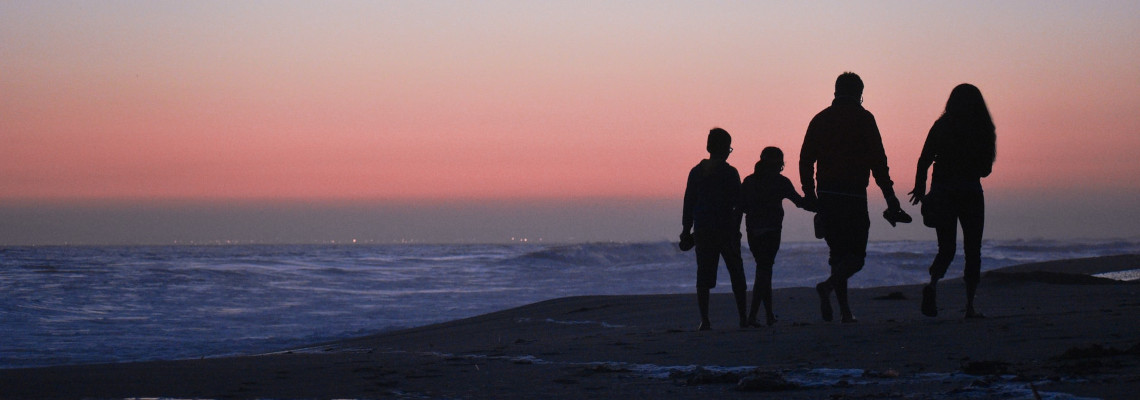 Família passeia à beira mar ao pôr do sol